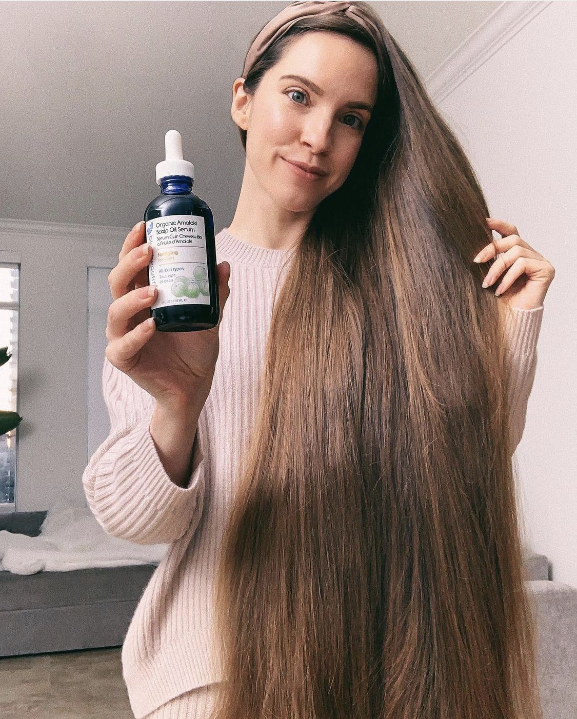 sarah nagel of holistic habits holding a bottle of blue beautifly amalaki scalp oil serum